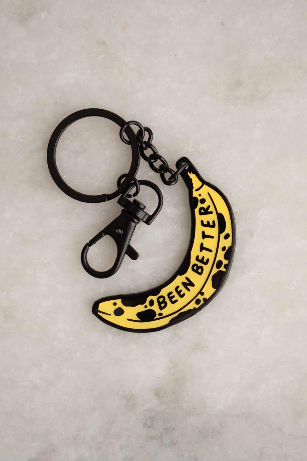 Enamel and metal keychain in the shape of a bruised banana featuring the phrase "been better"