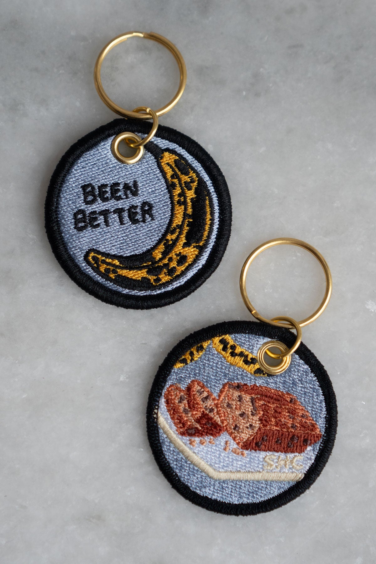 Embroidered keychain featuring a bruised banana and the phrase "been better" on one side, and banana bread on the reverse