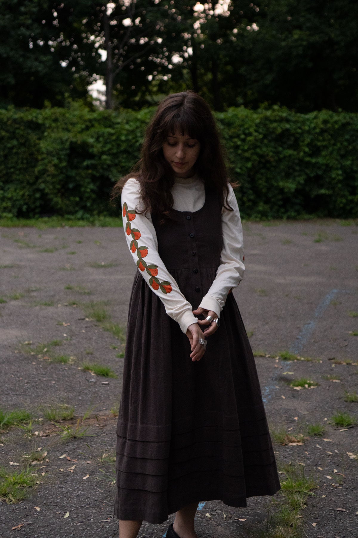 Woman wearing a brown dress layered over a cream long sleeved t-shirt featuring orange patterns outdoors.