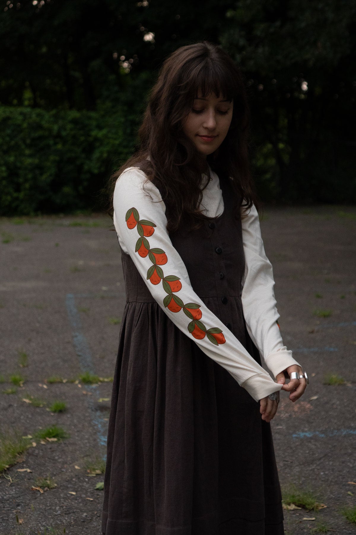 Woman wearing an off-white long-sleeve shirt with orange designs, standing outdoors.