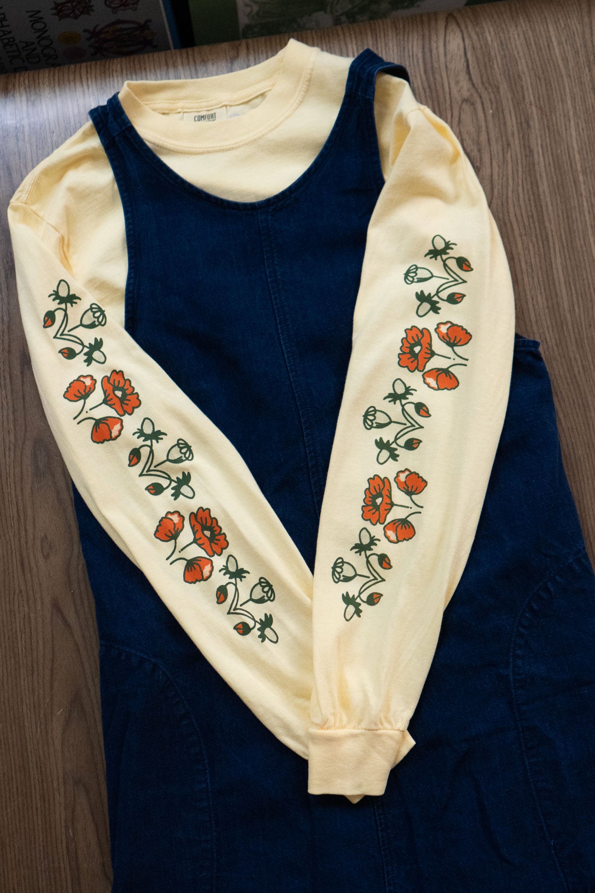Butter yellow long-sleeved t-shirt with orangey red and green poppy floral pattern layered under a denim pinafore dress