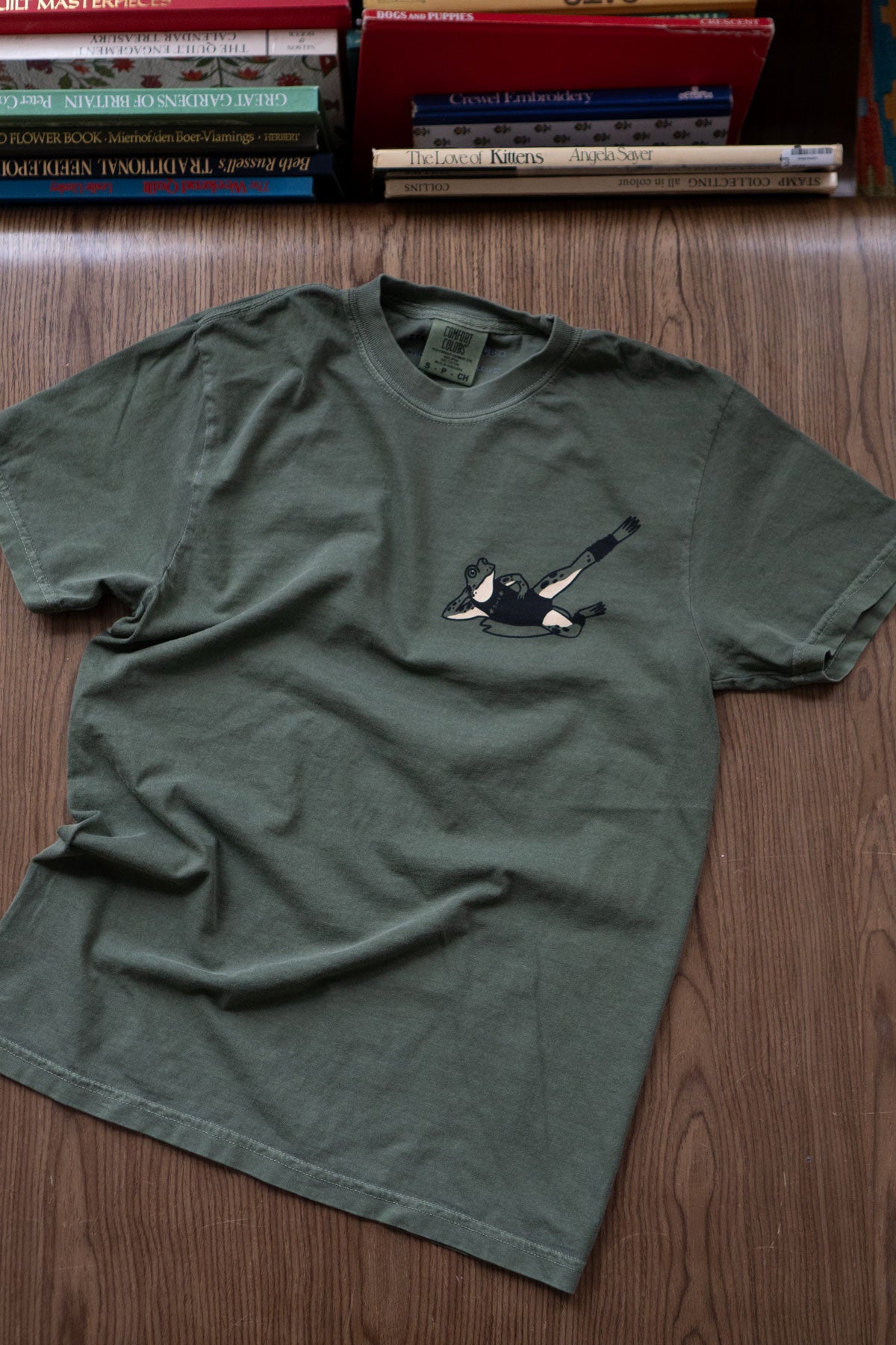 Green t-shirt featuring a printed frog exercising in '80s workout gear