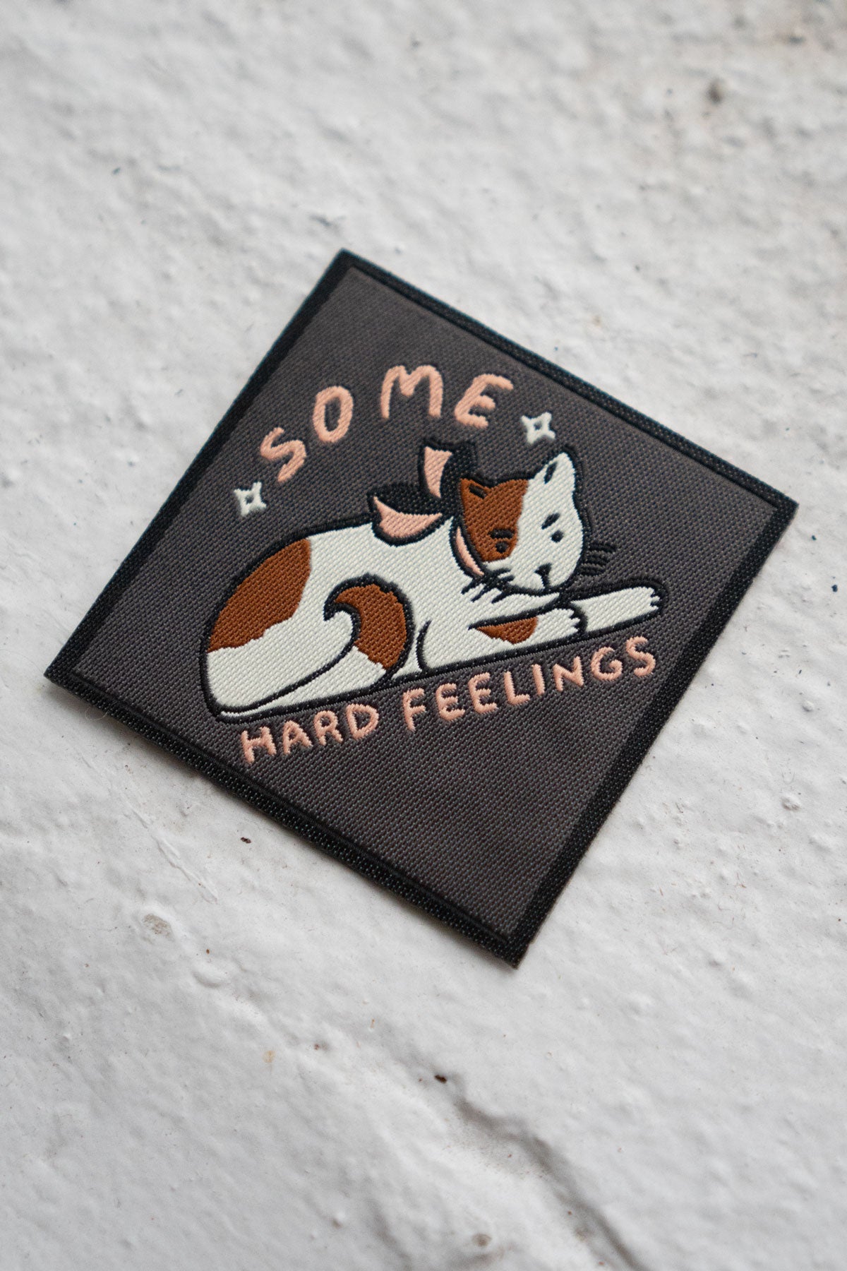 Woven patch with an image of a surly cat and the phrase "some hard feelings"