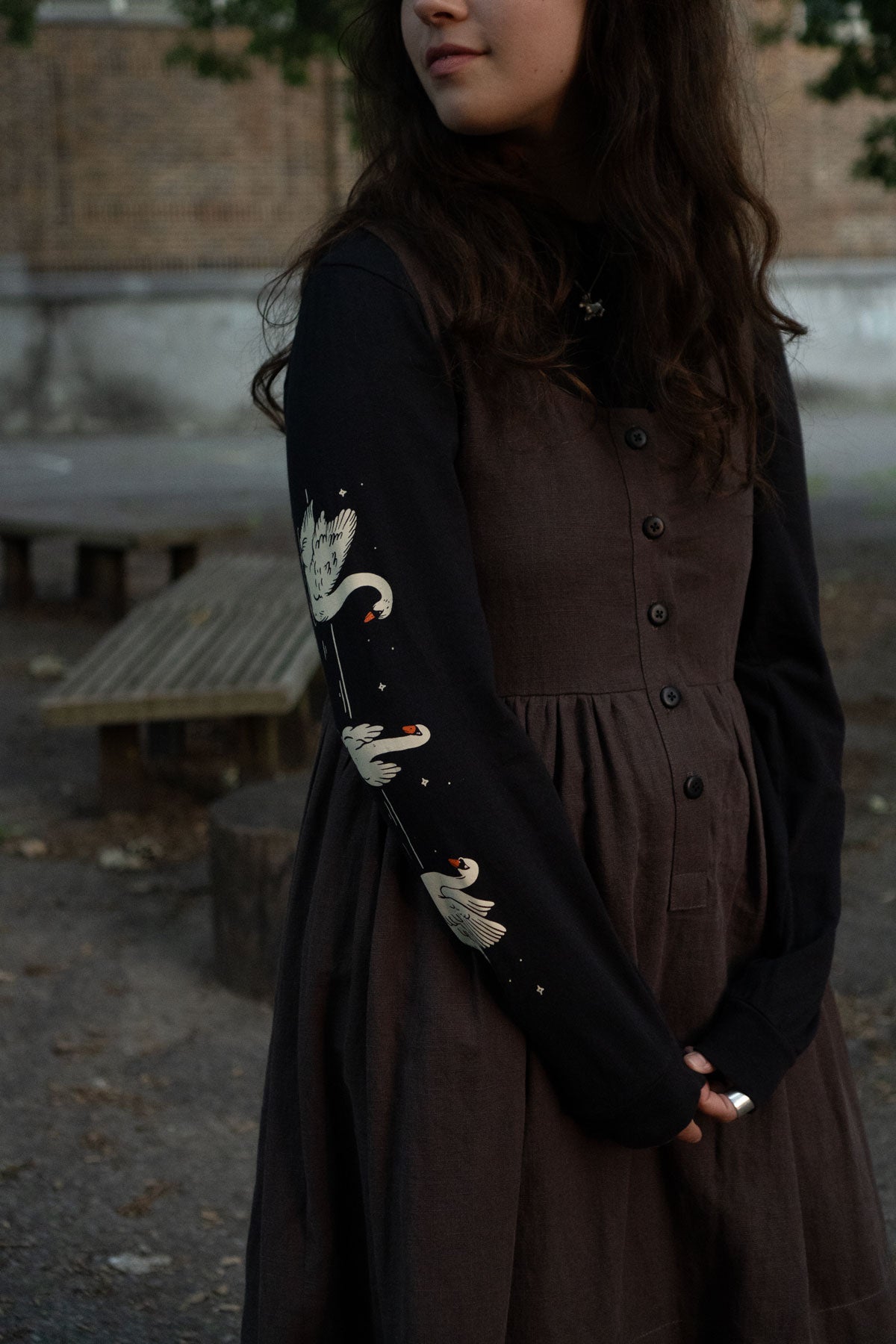 Woman wearing a brown dress and black long-sleeved tee with white swan print outdoors.