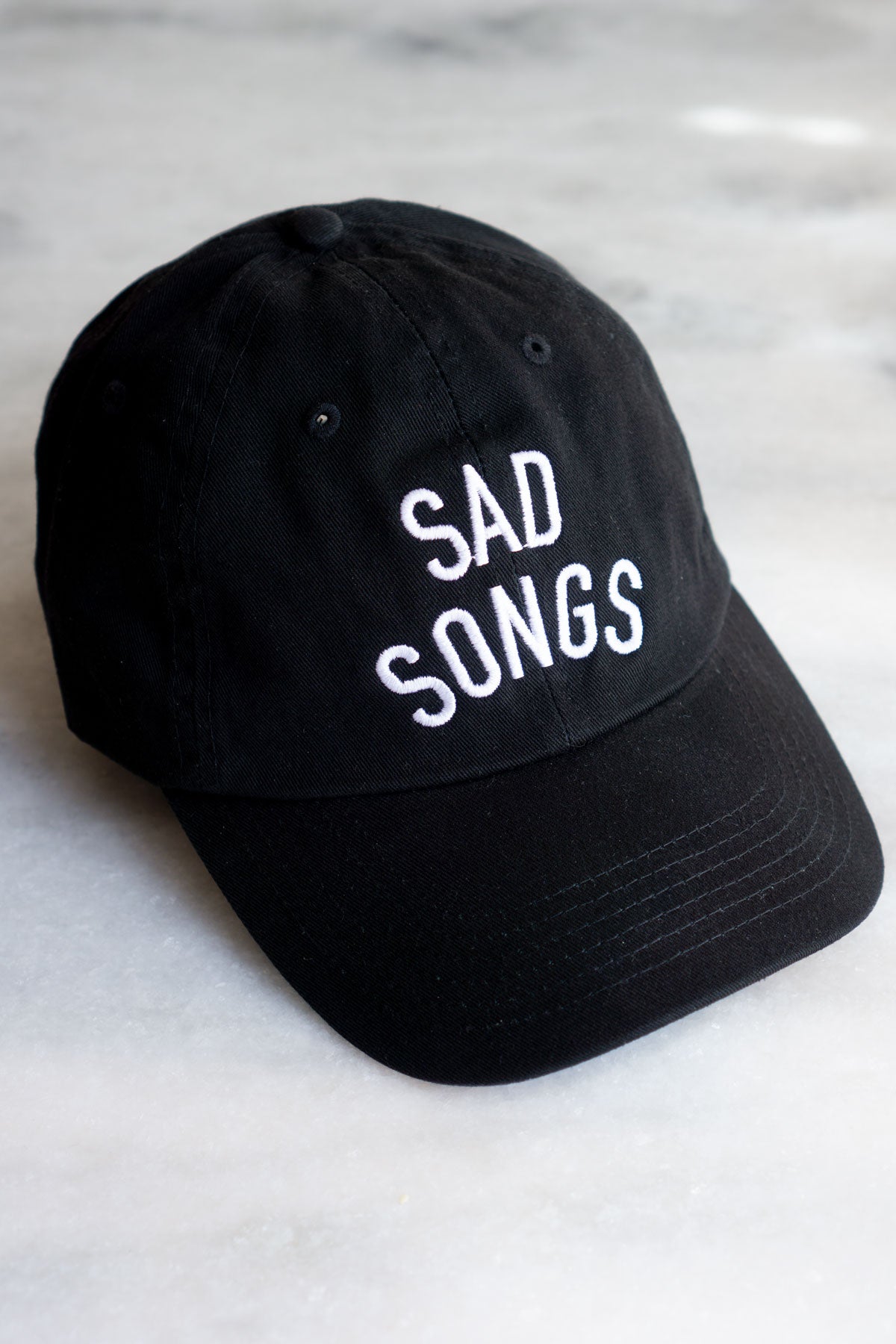 black baseball hat with white embroidered text reading SAD SONGS