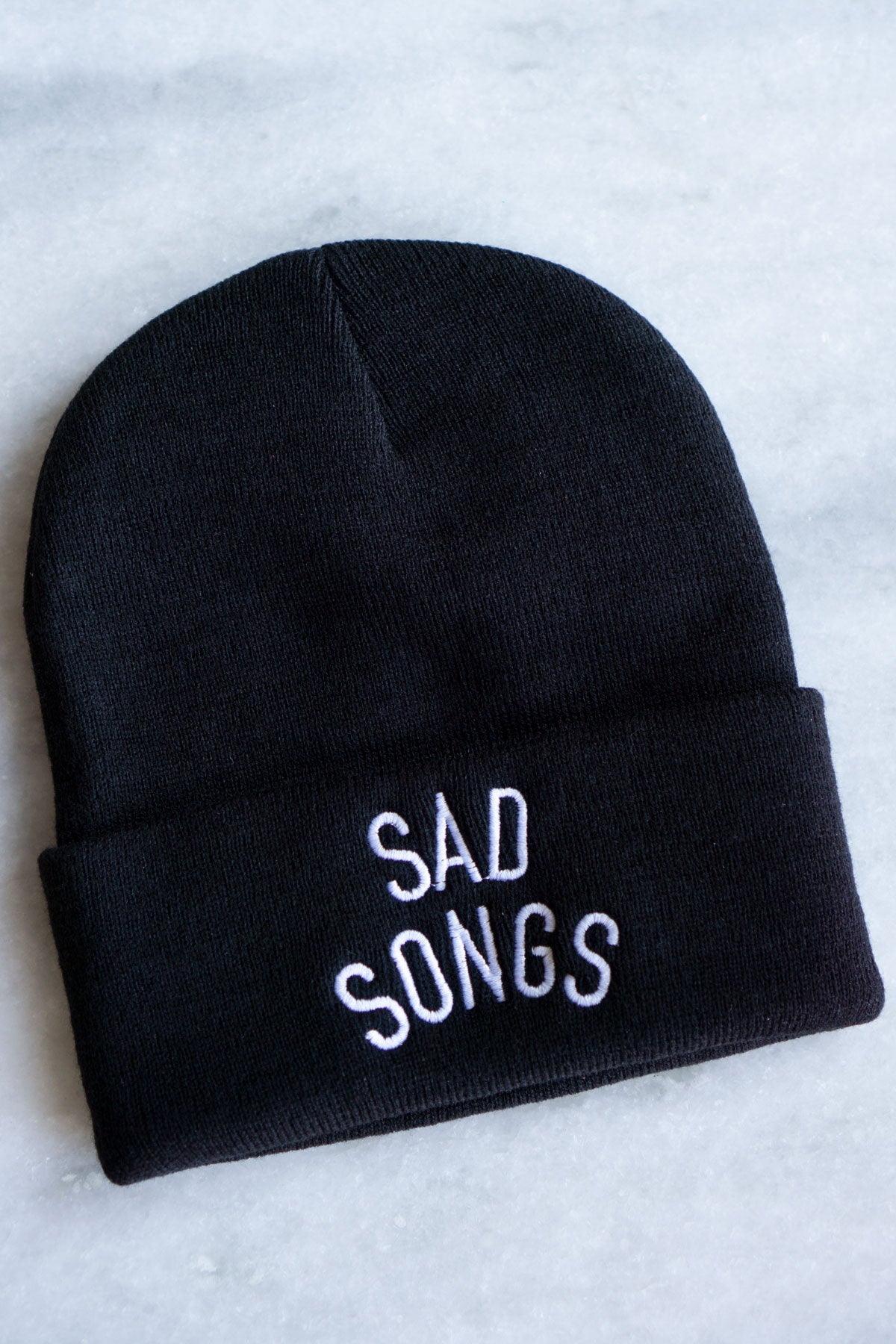 black beanie winter hat with sad songs in white font 
