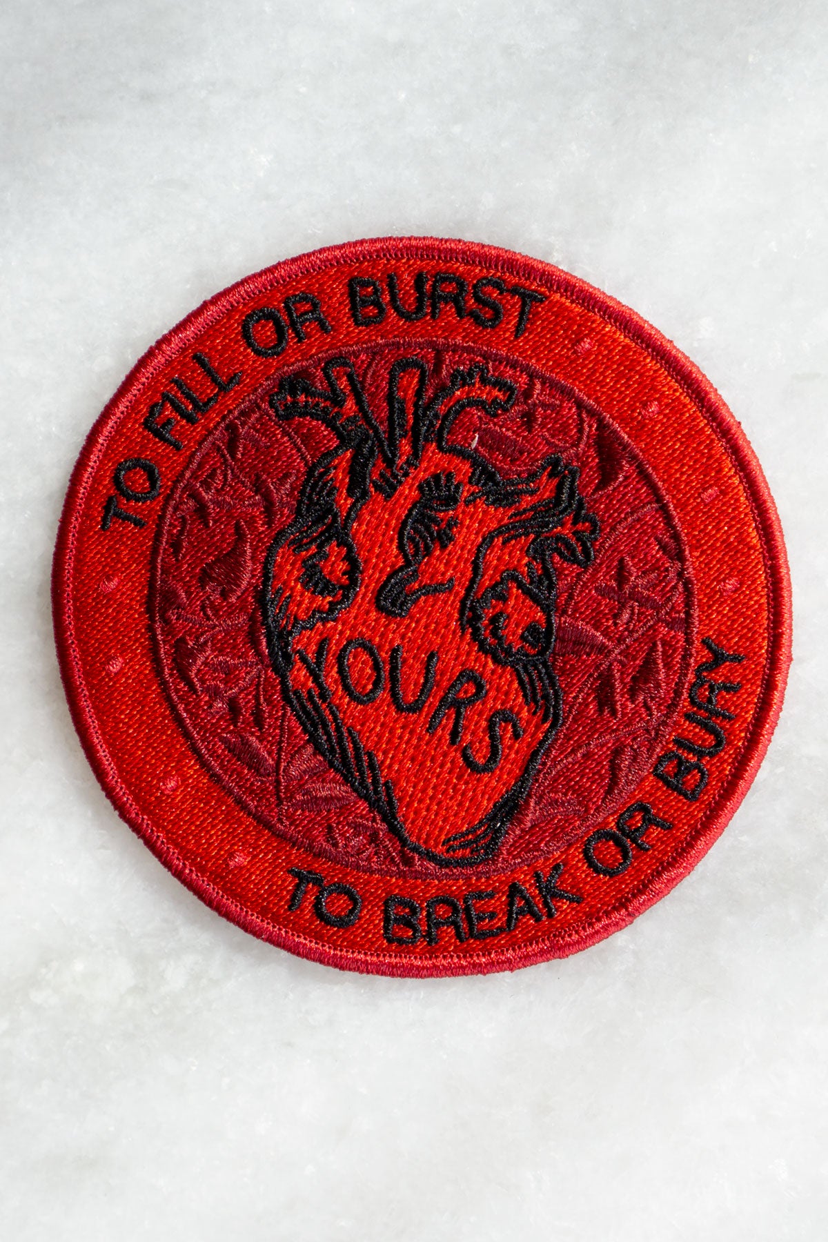 Round embroidered patch in shades of red featuring an anatomical heart and the Dashboard Confessional lyrics "to fill or burst - to break or bury"